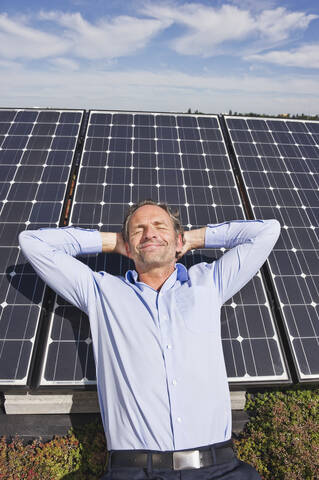 Deutschland, München, Älterer Mann, der lächelnd auf einem Panel in einer Solaranlage ruht, lizenzfreies Stockfoto