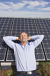 Deutschland, München, Älterer Mann, der lächelnd auf einem Panel in einer Solaranlage ruht - WESTF017877
