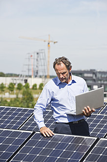 Deutschland, München, Älterer Mann mit Laptop in Solaranlage - WESTF017878