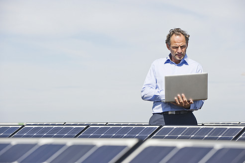 Deutschland, München, Älterer Mann mit Laptop in Solaranlage - WESTF017879