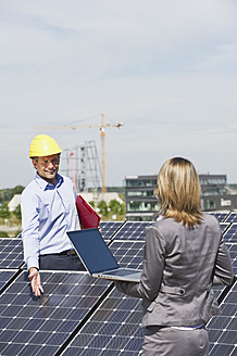 Deutschland, München, Ingenieure mit Laptop und Besprechung in einer Solaranlage - WESTF017889