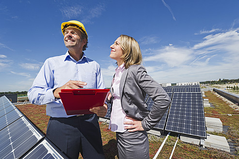 Deutschland, München, Ingenieure mit Klemmbrett in Solaranlage, lächelnd - WESTF017893