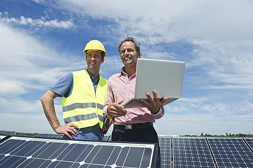 Deutschland, München, Ingenieure mit Laptop in Solaranlage - WESTF017895