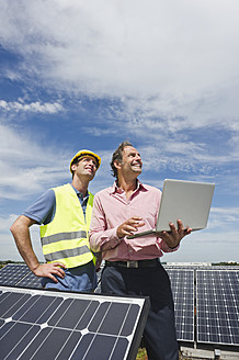 Deutschland, München, Ingenieure mit Laptop in Solaranlage - WESTF017896