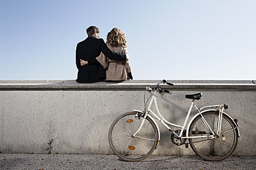 Germany, Bavaria, Munich, Young couple sitting on wall with bike - RBF000723