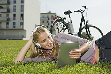 Deutschland, Bayern, Teenager-Mädchen benutzt Tablet-PC und hört Musik, lächelnd - RNF000697