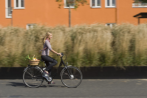 Germany, Bavaria, Teenage girl riding bicycle with basket, smiling - RNF000703