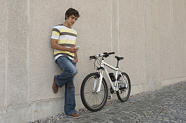 Deutschland, Bayern, Junger Mann telefoniert am Fahrrad stehend - RNF000710