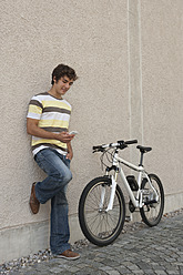 Germany, Bavaria, Young man using phone standing by bicycle, smiling - RNF000711