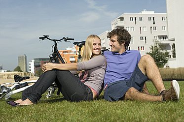 A happy couple enjoying the scenic beauty of Bavaria, Germany while sitting on the lush green grass - RNF000722