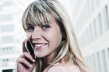 A cheerful young woman in Cologne, Germany, smiling while using her mobile phone in a portrait - WESTF017930