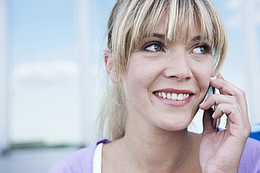 Junge Frau aus Köln lächelt glücklich in die Kamera, während sie ihr Handy benutzt - WESTF017938