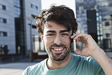 Junges Mann mit Handy lächelt in Köln, Deutschland - ein Porträt voller Lebensfreude - WESTF017976