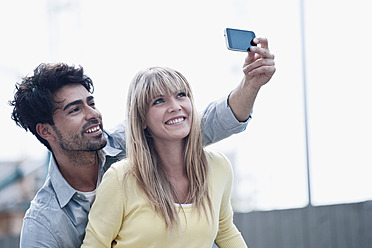 Smiling young couple in Cologne, Germany, use their cell phone to capture a photo - WESTF018011