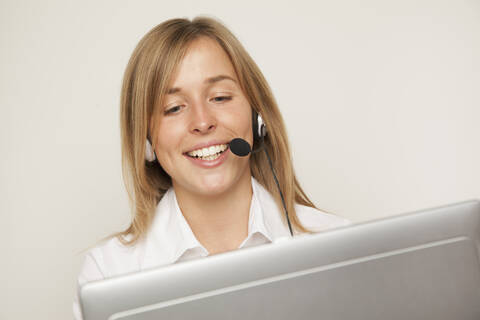 Junge Frau mit Headset am Computer, lächelnd, lizenzfreies Stockfoto