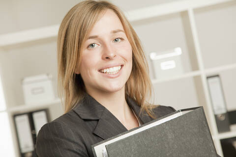 Junge Frau mit Ordner im Büro, lächelnd, Porträt, lizenzfreies Stockfoto