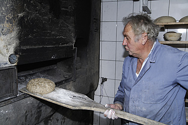 Ein älterer Mann backt Brot in einer traditionellen Holzofenbäckerei in Egling, Oberbayern, Deutschland - TCF001941