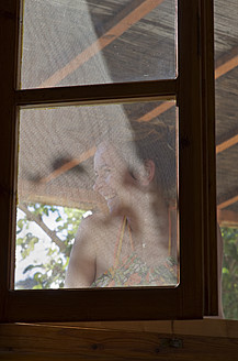 A happy woman enjoying the fresh air on Ithaca Island, Greece, standing near a fly screen - MUF001170