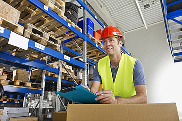 A cheerful Munich warehouse worker poses with a clipboard against the stunning backdrop of Bavarian scenery - WESTF018034