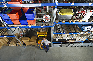 A man stands by a pallet transporter in a Munich warehouse, highlighting the busy industrial atmosphere of Bavaria, Germany - WESTF018049