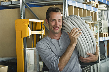 Ein fröhlicher bayerischer Arbeiter in München, Deutschland, trägt einen Plastikschlauch mit einem Lächeln im Gesicht - WESTF018053