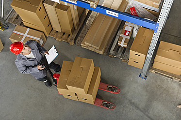 A warehouse worker in Munich, Germany checks inventory using a clipboard in a Bavarian setting - WESTF018060