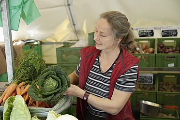Eine Frau wählt auf einem Markt in Wolfratshausen, Oberbayern, Deutschland, mit großer Sorgfalt und Aufmerksamkeit frische Produkte aus - TCF002102