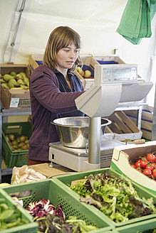 Eine junge Frau wählt auf einem lebhaften Markt in Wolfratshausen, Oberbayern, Deutschland, sorgfältig frische und gesunde Produkte aus - TCF002114