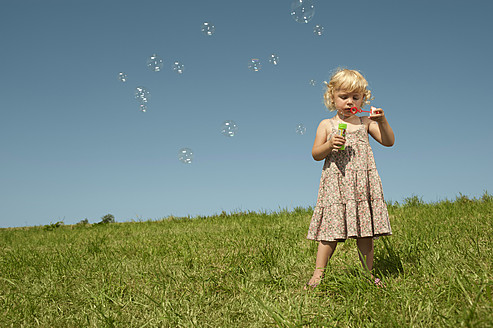 Ein junges bayerisches Mädchen genießt einen schönen Tag, indem es in der malerischen deutschen Landschaft Seifenblasen pustet - RNF000735