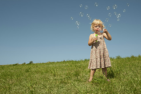 A cheerful Bavarian girl enjoys a sunny day while blowing soap bubbles with pure joy - RNF000736
