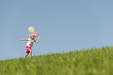 A joyful young woman sprints through a picturesque Bavarian meadow, holding a colorful bunch of balloons and grinning from ear to ear - RNF000737