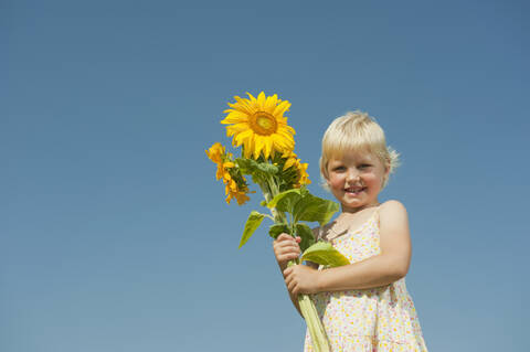 Ein strahlendes bayerisches Mädchen hält eine Sonnenblume in der Hand und strahlt pure Freude in diesem atemberaubenden Porträt aus., lizenzfreies Stockfoto