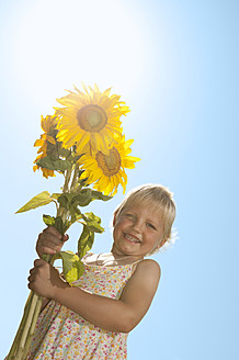 Ein bayerisches Mädchen mit einer leuchtenden Sonnenblume strahlt auf diesem fröhlichen Foto Glück und Wärme aus. - RNF000743
