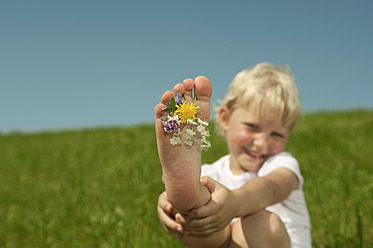 Ein bayerisches Mädchen genießt das Gefühl von Blumen unter den Füßen und spielt auf dem leuchtend grünen Gras in einem atemberaubenden Porträt - RNF000752
