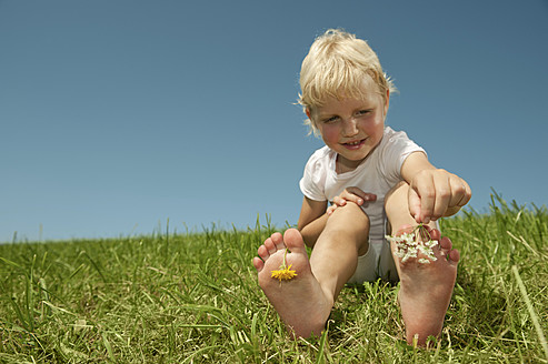 A Bavarian girl enjoys playing with flowers, smiling on the grass with blooming toes, radiating pure joy - RNF000753