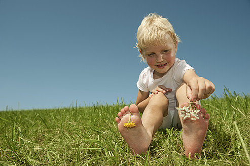 Ein bayerisches Mädchen genießt es, mit Blumen zu spielen, lächelt mit blühenden Zehen im Gras und strahlt pure Freude aus - RNF000753