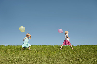 Drei glückliche Mädchen genießen die bayerische Sonne und schlendern durch grüne Felder, die mit bunten Luftballons geschmückt sind - RNF000755