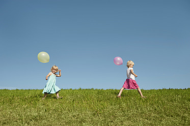 Three happy girls enjoy the Bavarian sunshine, strolling through verdant fields adorned with colorful balloons - RNF000755