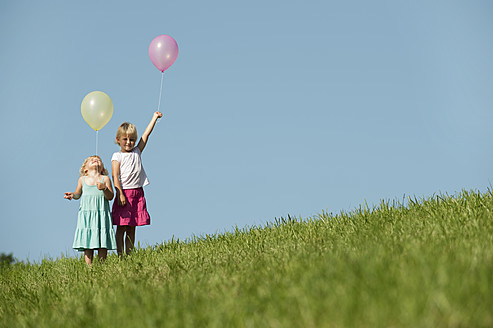 Drei fröhliche Mädchen genießen den bayerischen Sonnenschein und halten bunte Luftballons in einem üppigen grünen Feld - RNF000756