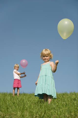 Drei junge Mädchen genießen die bayerische Sonne und halten bunte Luftballons in einer üppigen grünen Landschaft, lizenzfreies Stockfoto