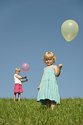 Drei junge Mädchen genießen die bayerische Sonne und halten bunte Luftballons in einer üppigen grünen Landschaft - RNF000757