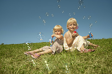 Three young girls enjoy a sunny day in Bavaria, sitting on the grass and playing with bubbles - RNF000759