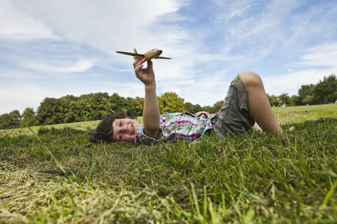 Fröhlicher Junge, der einen spielerischen Tag in einem bayerischen Park genießt und mit einem breiten Lächeln ein Modellflugzeug steuert, lizenzfreies Stockfoto