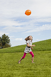 Ein glückliches Mädchen genießt den sonnigen Tag in einem bayerischen Park und spielt voller Freude mit einem bunten Luftballon - SKF000552