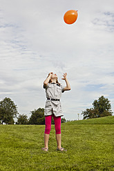 Ein glückliches kleines Mädchen genießt den sonnigen Tag in einem bayerischen Park und spielt vergnügt mit einem bunten Luftballon - SKF000553