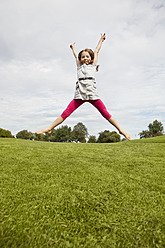 Ein fröhliches junges Mädchen hüpft ausgelassen in einem schönen bayerischen Park, festgehalten in einem lebendigen und farbenfrohen Porträt. - SKF000555