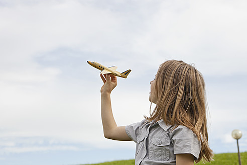 Ein fröhliches junges Mädchen genießt einen sonnigen Tag in Bayern, Deutschland, beim Spielen mit einem Modellflugzeug im Park - SKF000558