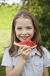 Ein bayerischer Park bietet die perfekte Kulisse für ein glückliches Mädchen, das mit Freude ein erfrischendes Stück Wassermelone genießt. - SKF000561