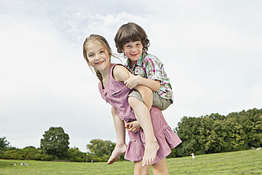 Eine Gruppe glücklicher Kinder, die sich in einem bayerischen Park vergnügen, wobei ein Mädchen spielerisch einen lächelnden Jungen trägt - SKF000566