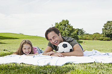 Father and daughter enjoy a sunny day in Bavaria, bonding over a joyful moment while relaxing on the lush greenery - SKF000580